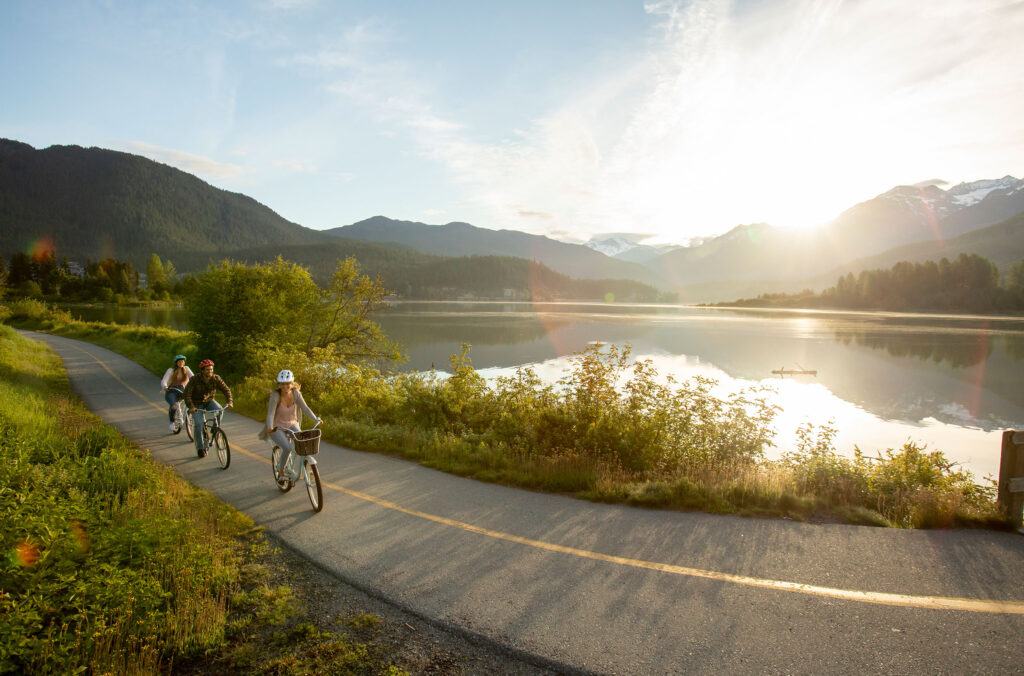 Three people ride cruiser bikes along Whistler's Valley Trail close to Green Lake in the sunshine.