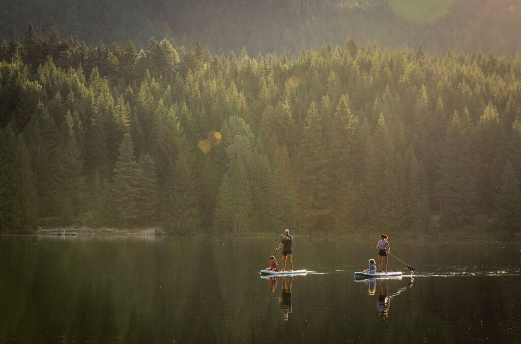 A family stand up paddle board on the mirror-like waters of Lost Lake in Whistler.