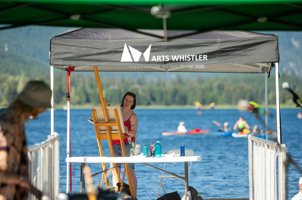 A painter works away while floating on a lake dock in Whistler.