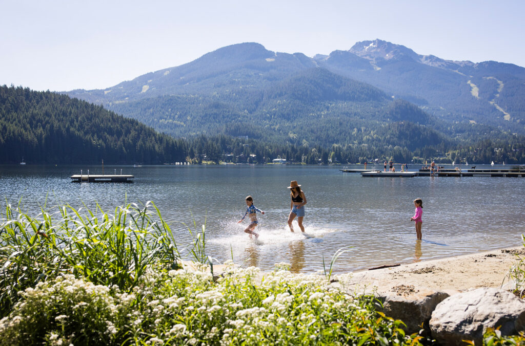 A mom and her two children play in the shallows of Alta Lake at Rainbow Park in Whistler under the summer sun.
