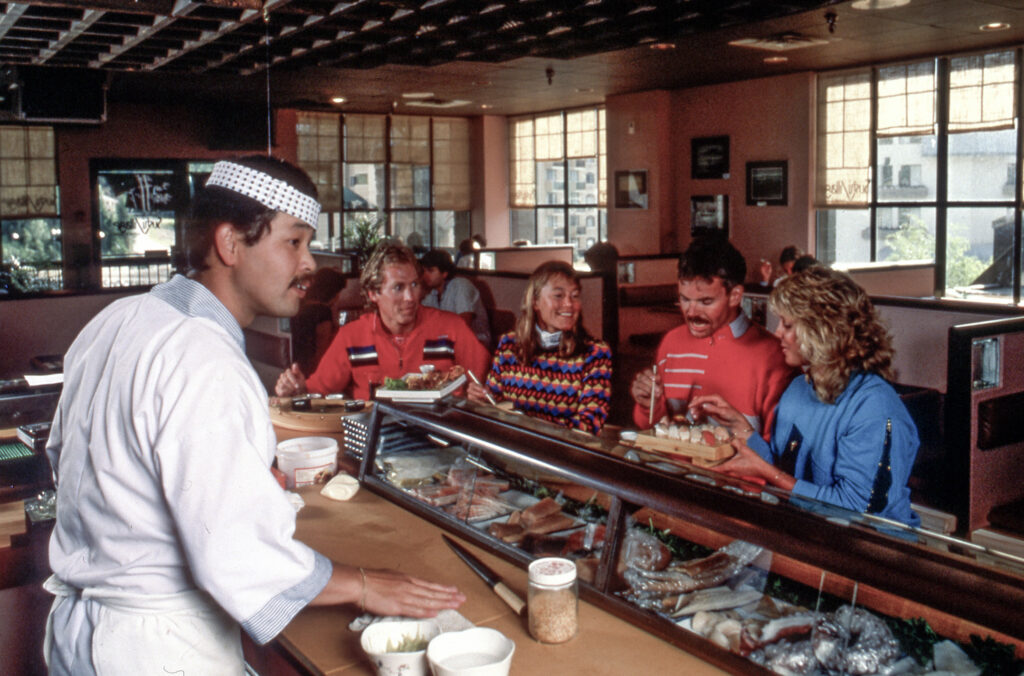Four people sit eating sushi at Sushi Village with the chef serving them at the bar area.