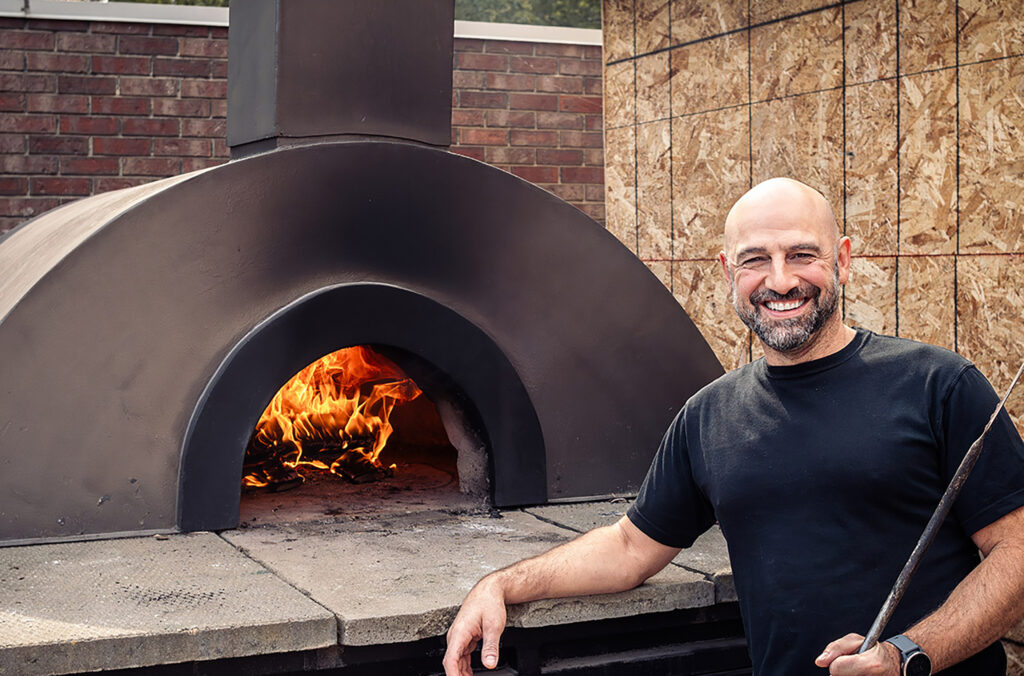 Chef Jason Dabbagh stands in front of an outdoor pizza oven.