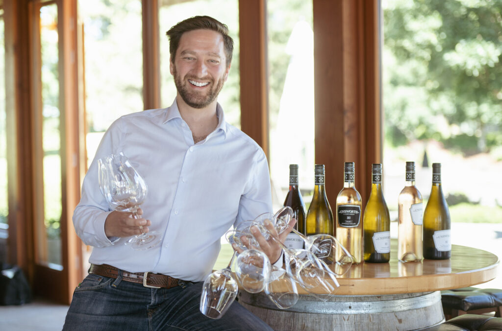 Chris Turyk holds wine glasses as he leans on a barrel.