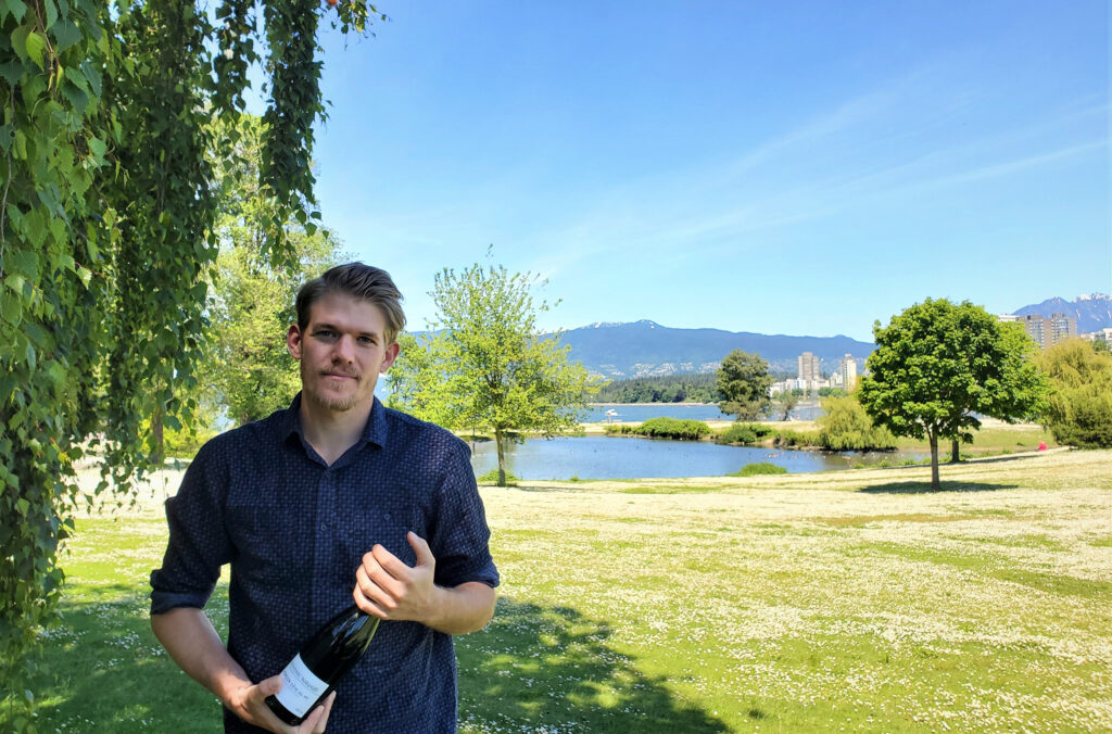 Ian holds a bottle of wine while stood outside at an event. 