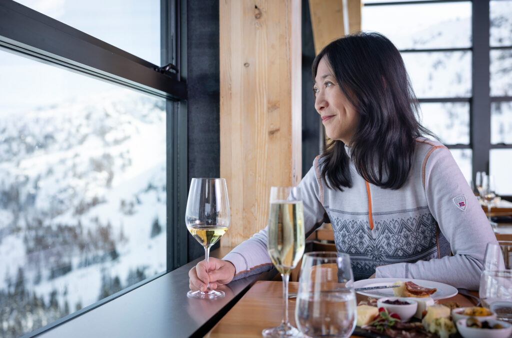A person gazes out over Blackcomb Mountain while enjoying food and a glass of white wine.
