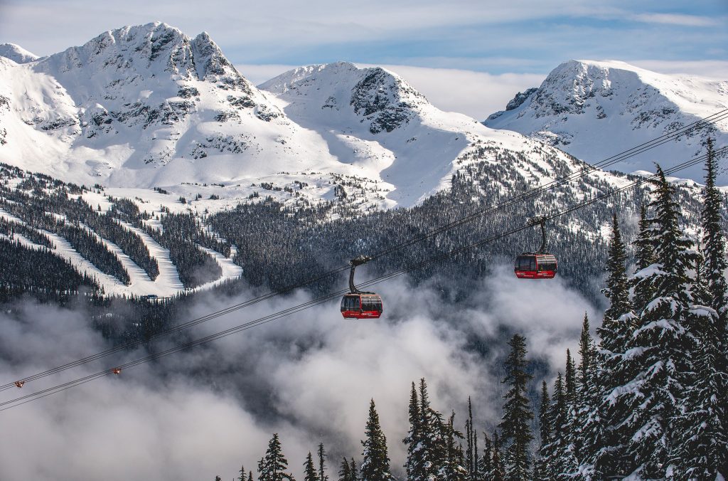 Two red cabins of the PEAK 2 PEAK Gondola on a clear, snowy day travel across the Whistler Valley.