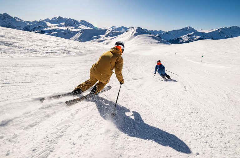 Two skiers make their way down a groomed slope on Whistler Mountain in the winter sunshine.