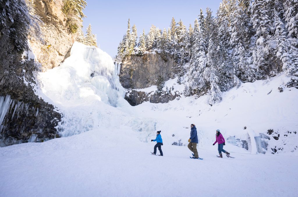 Three snowshoers explore the base of Alexander Falls in Whistler.