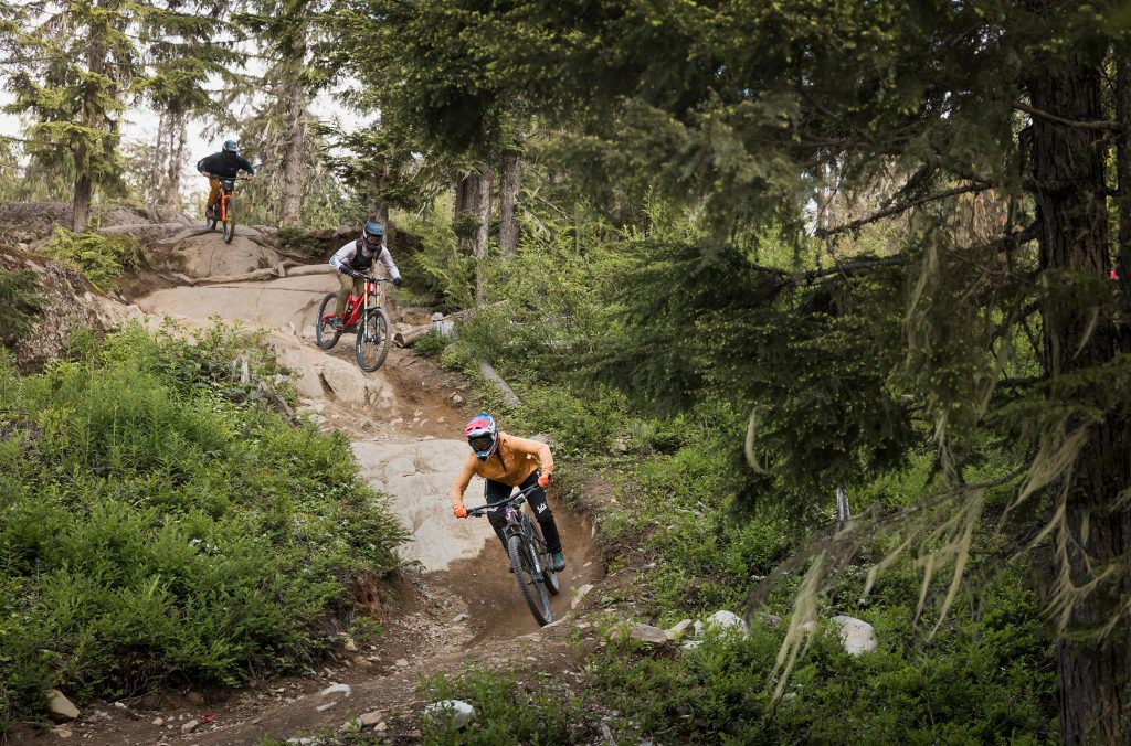 Three bikers ride down a rock roll in Whistler Mountain Bike Park.