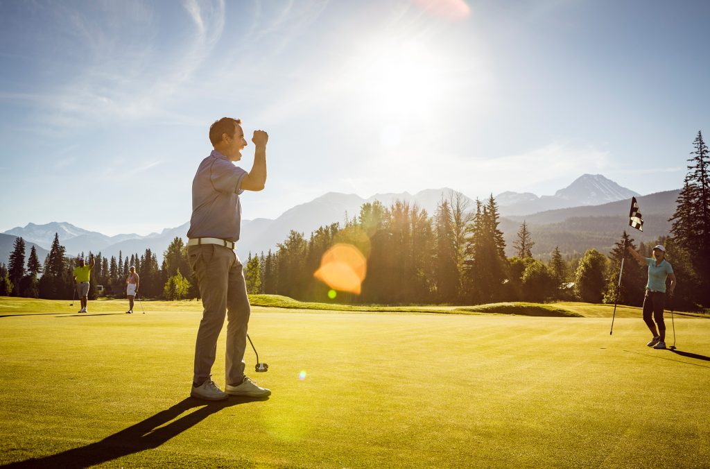 A group of four golfers celebrate a good shot on a sunny Whistler golf course.