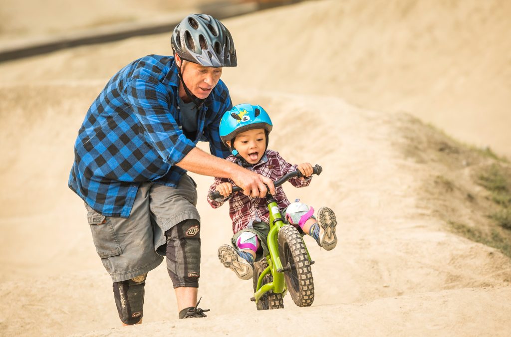 An adult helps a child ride on the pump track in Whistler.