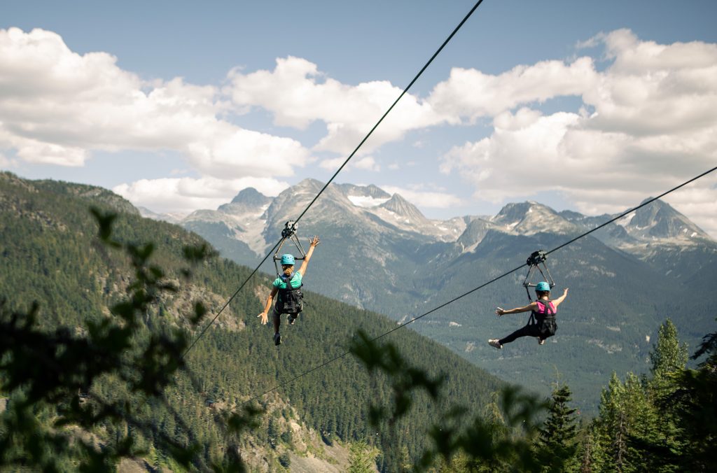 Two people zipline across a valley in Whistler in spring. 