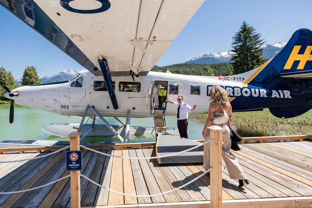 A float plane is docked at Green Lake in Whistler as a passenger walks across a wooden boardwalk in the sun to get in. 