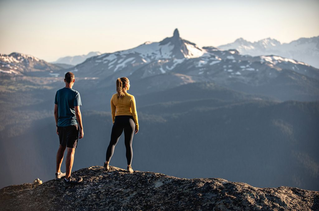 Two people look out toward Black Tusk from Whistler Mountain in the summer.