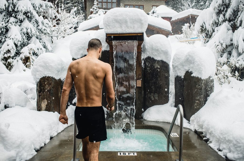 A person is entering one of the Scandinave Spa's cold waterfalls surrounded by snow.