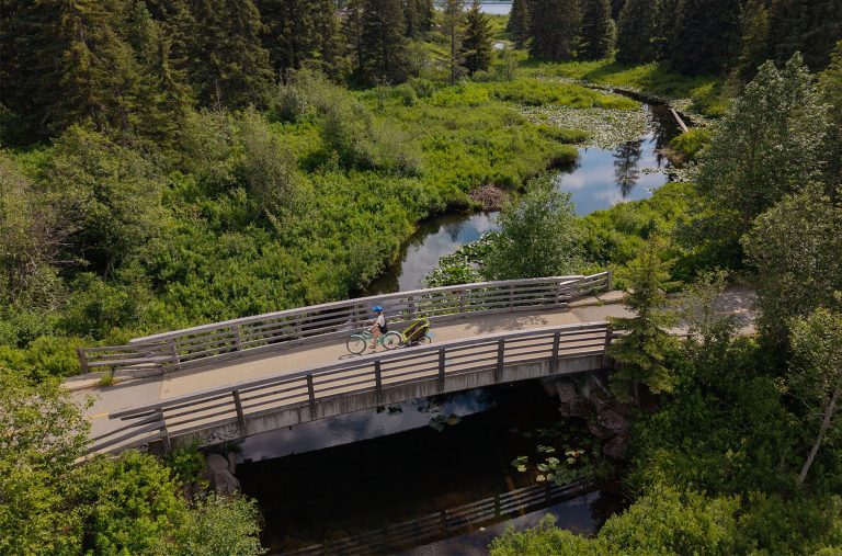 A rider pulled a chariot over a bridge with the Fitzsimmons Creek flowing beneath it in Whistler, along the Valley Trail.