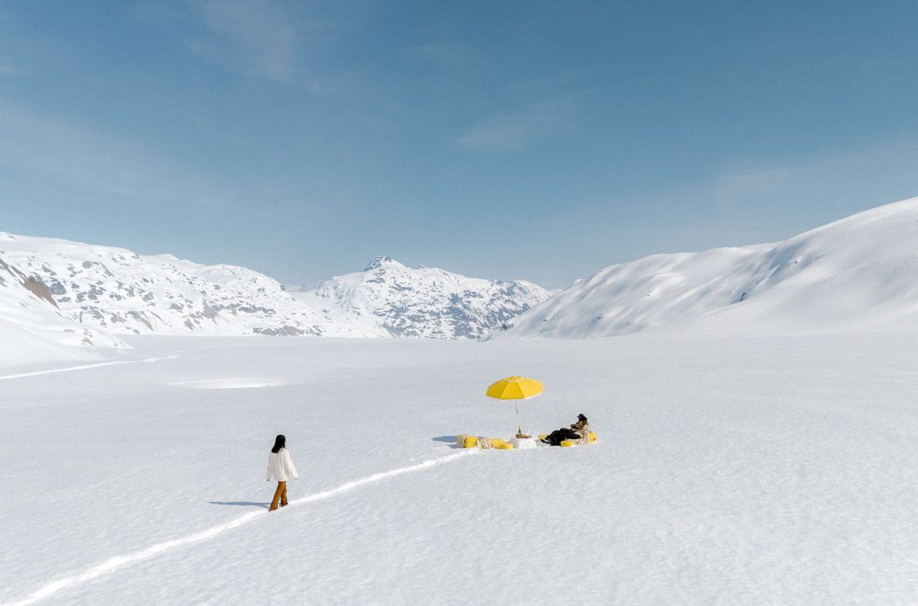 A person walks across a snowy glacier to seating where they are having apres after visiting the ice caves in Whistler.