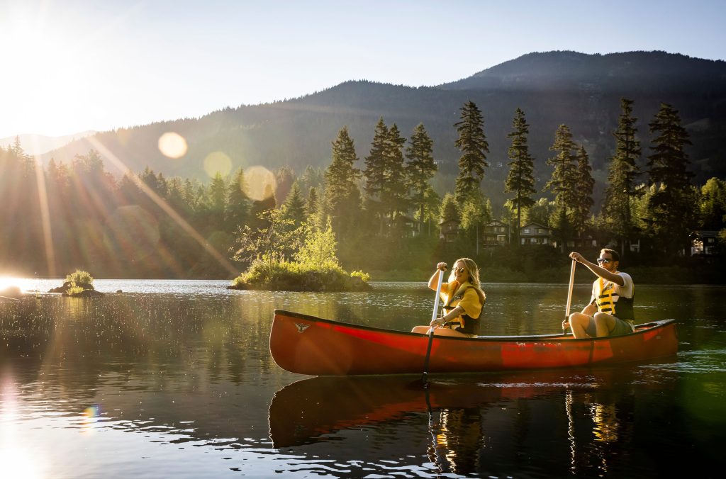 Two people paddle in a canoe on a Whistler lake in the summer as the sun starts to set.