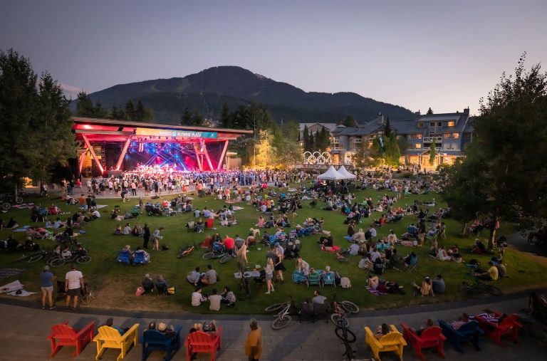 A crowd listens to the music at an outdoor concert in the summer in Whistler in the evening.