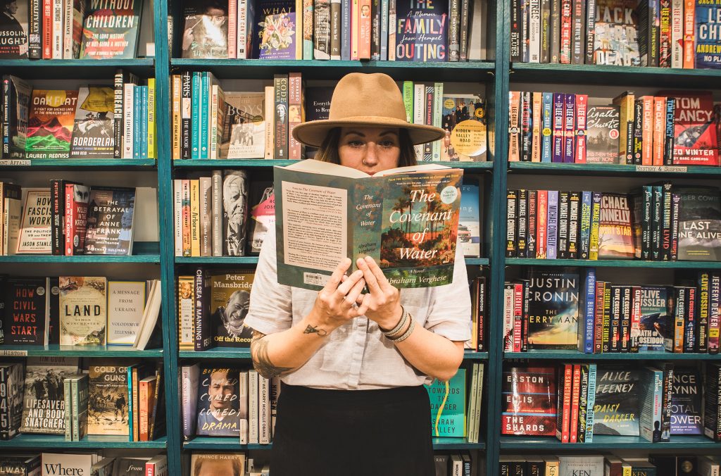 Sarah, the owner of Armchair Books in Whistler stands reading a book in front of the bookcases.