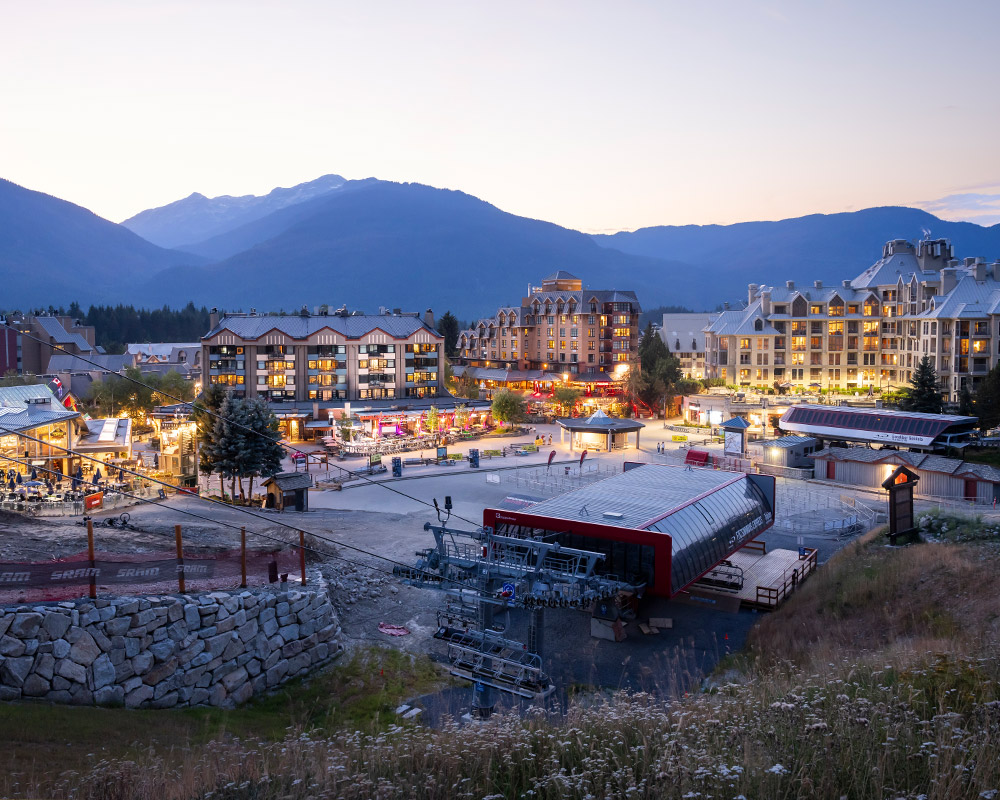 Whistler Village glows at dusk, nestled between towering mountains with bike-friendly accommodation just steps from the gondola. A vibrant atmosphere welcomes adventurers, whether hitting the trails or unwinding after a day of riding.