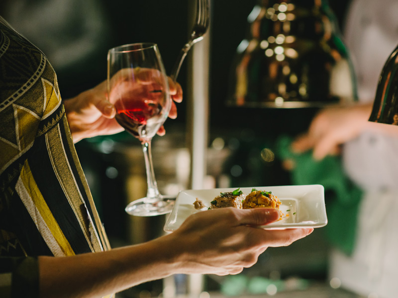 Guest enjoys a glass of wine and a plated tasting dish at the Cornucopia Night Market in Whistler.
