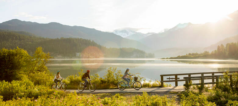 Three people riding bikes on the Valley Trail by Green Lake on a beautiful spring day in the mountains of Whistler.