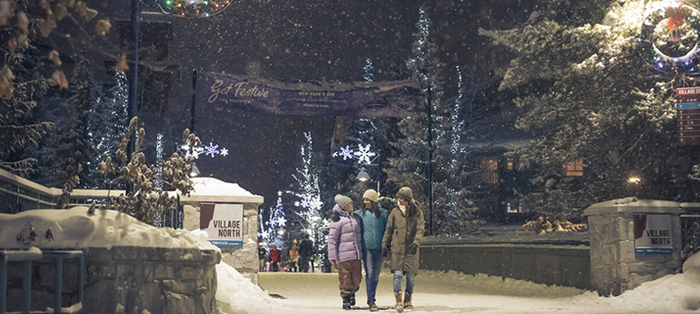 Three people walking on Whistler Village Stroll in the snow at Christmas