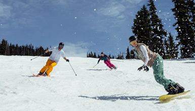 Three people skiing and snowboarding in 7th Heaven on Blackcomb Mountain on a sunny spring day