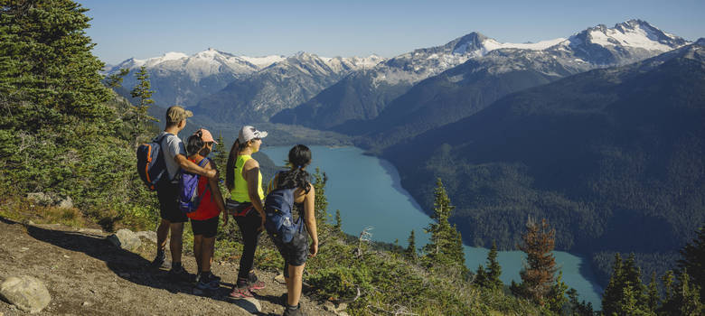 A group of hikers admiring the view of Cheakamus Lake from the High Note Trail on Whistler Mountain on a sunny summer day.
