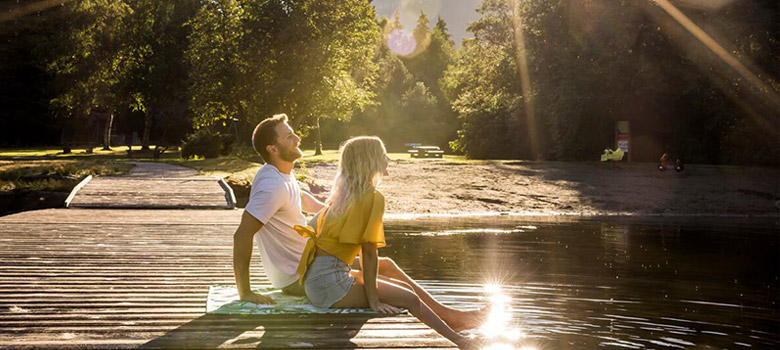 A couple sitting on a dock at a lake in Whistler Creekside with sun filtering through the trees