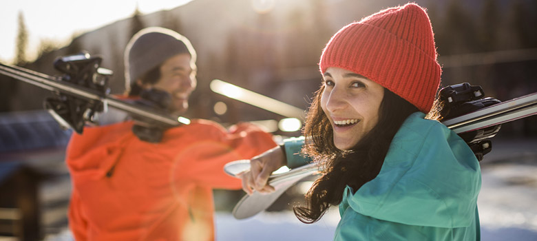 Two skiers, glowing in the golden light of a spring afternoon in Whistler, carry their gear off the slopes, heading to après after an epic day in the mountains.