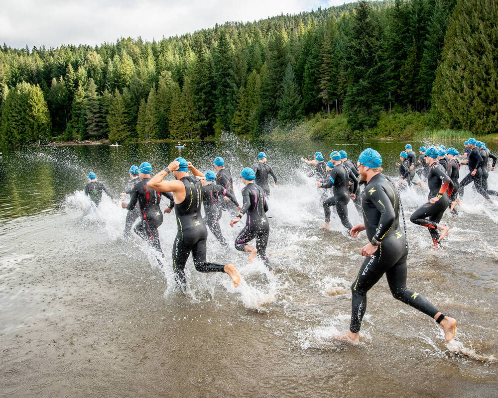Participants in the Whistler X Tri running into the lake wearing wetsuits in Whistler