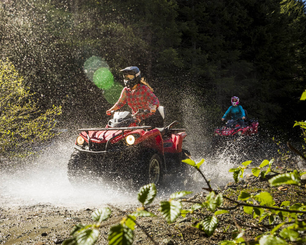 Two women on a guided ATV tour blasting through a puddle in the Whistler backcountry.