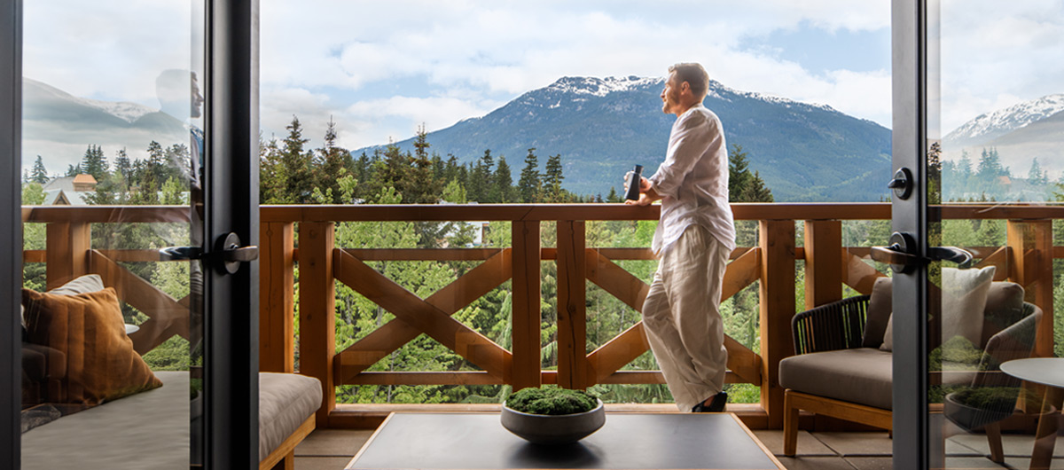Guest enjoying coffee on a private balcony overlooking Whistler Mountain and forest from a luxury accommodation in Whistler, BC.