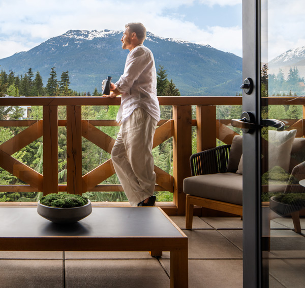 Guest enjoying coffee on a private balcony overlooking Whistler Mountain and forest from a luxury accommodation in Whistler, BC.