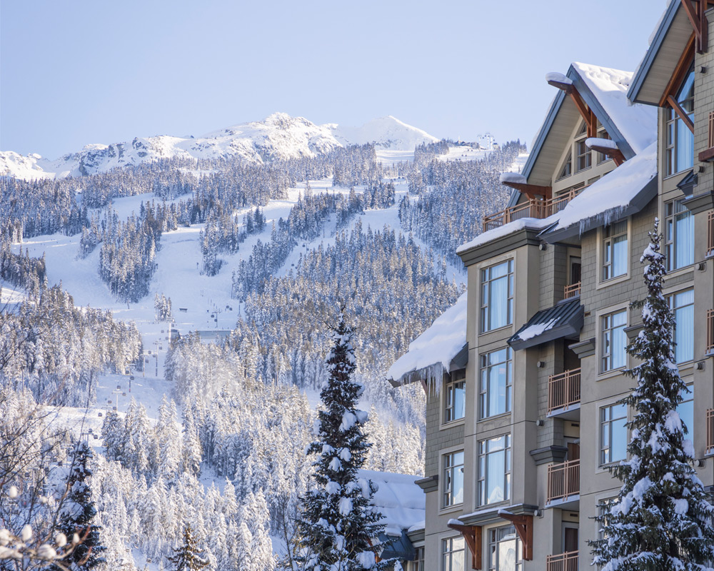 A snow-covered hotel beside the ski runs, with snowy forest and the mountain behind
