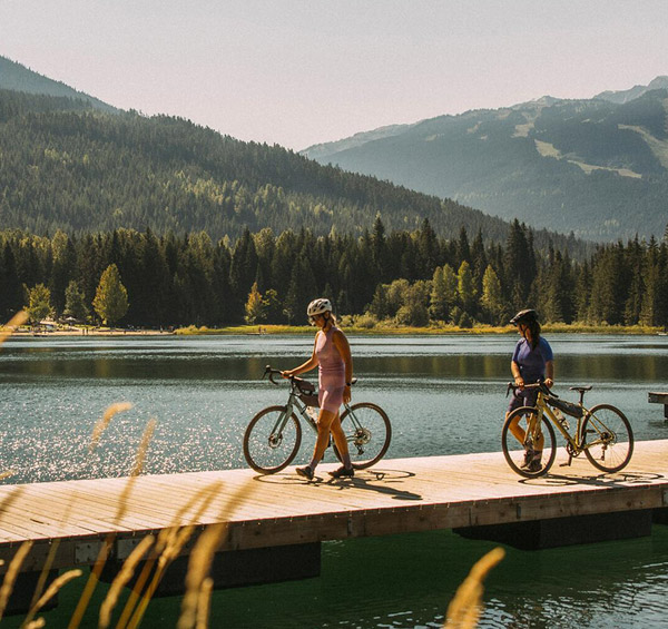 Two gravel riders on the dock overlooking Lost Lake on a sunny summer day in Whistler, British Columbia