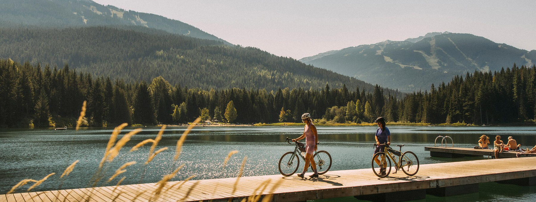 Two gravel riders on the dock overlooking Lost Lake on a sunny summer day in Whistler, British Columbia