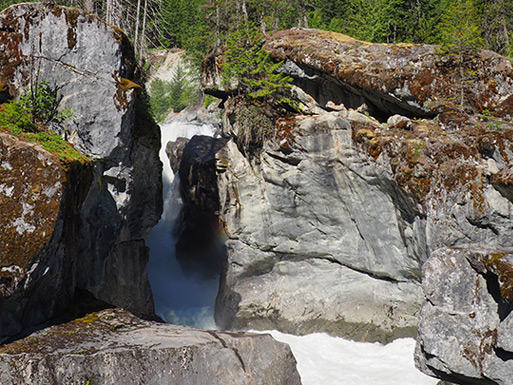 Visitors standing near the powerful Nairn Falls surrounded by forest and mountain scenery.