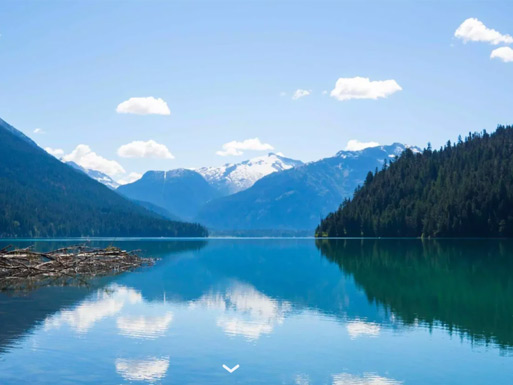 Hikers walking beside turquoise Cheakamus Lake surrounded by forested mountain ridges.
