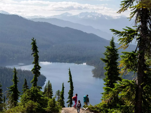 Hikers beside the turquoise waters of Garibaldi Lake with glaciers and mountain peaks beyond.