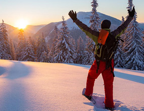 Snowshoeing in Whistler at sunrise, with a winter adventurer standing on a snowy mountain ridge overlooking forested alpine peaks.