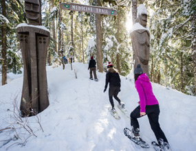 Snowshoeing on the Medicine Trail in Whistler, as a group walks through a snowy forest past carved wooden figures.