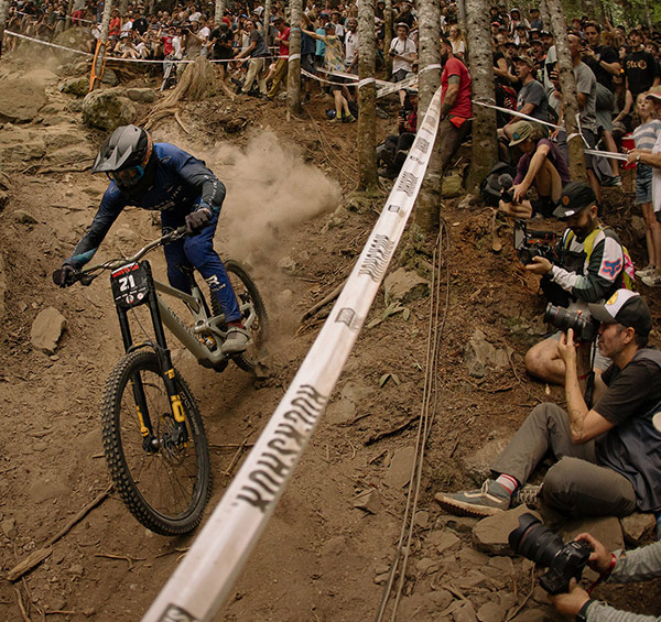 A downhill mountain bike athlete racing 1199 in Whistler with spectators cheering them on during Crankworx.
