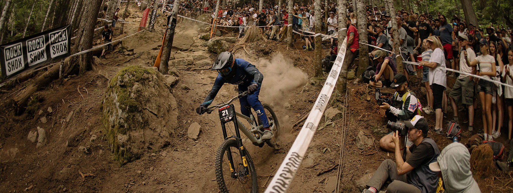 A downhill mountain bike athlete racing 1199 in Whistler with spectators cheering them on during Crankworx.