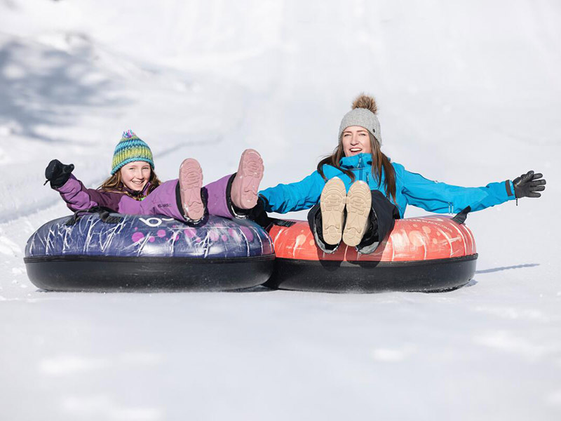 A family smiling while sliding on snow tubes at the tube park in Whistler