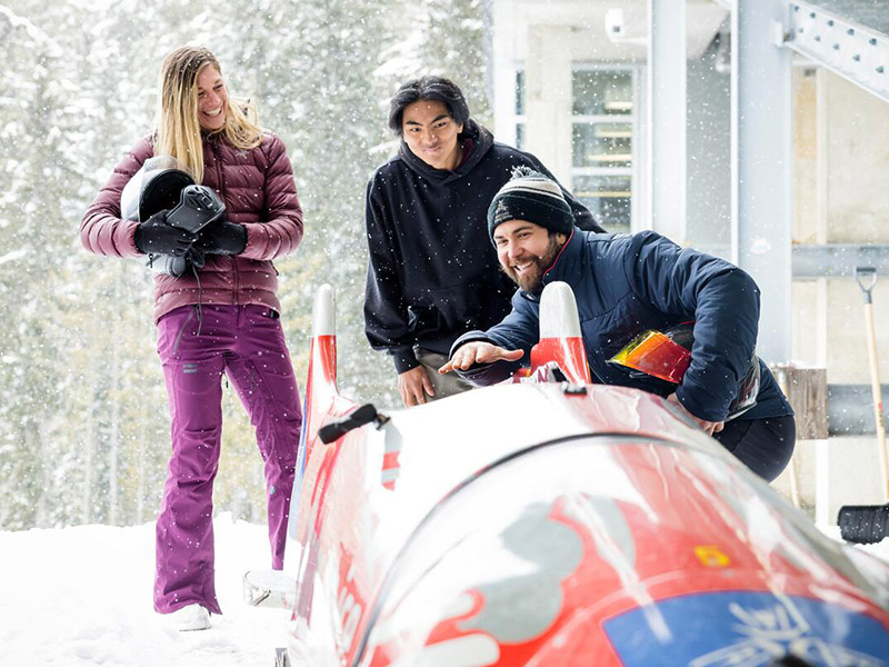 A couple getting a tour of a bobsleigh at Whistler Sliding Centre as snow falls down around them