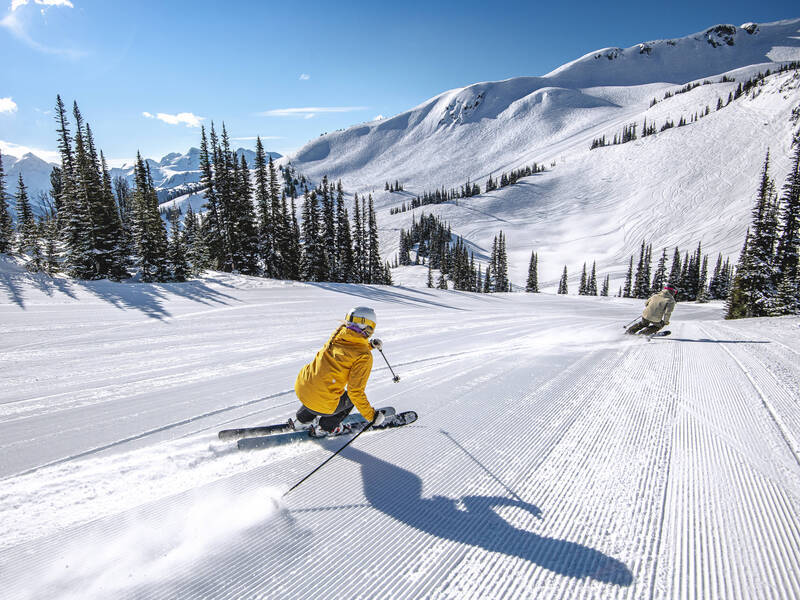 Two skiers carving on a perfectly groomed run in springtime at Whistler Blackcomb