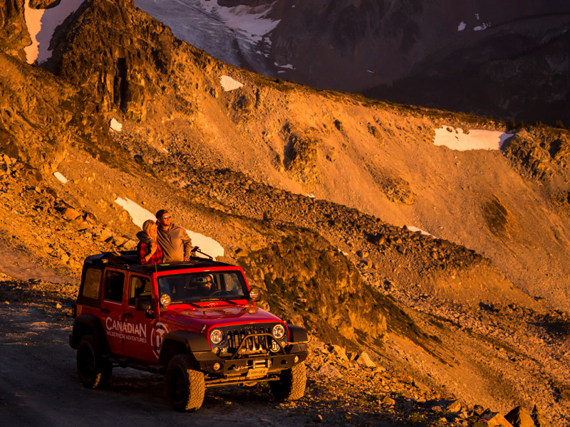 Blackcomb Sunset 4x4 Tour in Whistler BC, with guests riding a red off-road vehicle along an alpine mountain road during sunset overlooking the Coast Mountains.